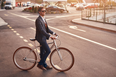 Cheerful trendy businessman with bicycle on streetの写真素材