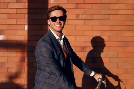 Cheerful modern entrepreneur on city bicycle in sunlightの写真素材