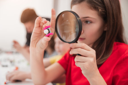 Schoolgirl with magnifier examining detail during robotics classの写真素材