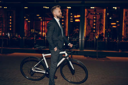 Classy businessman with bicycle standing on night city streetの写真素材