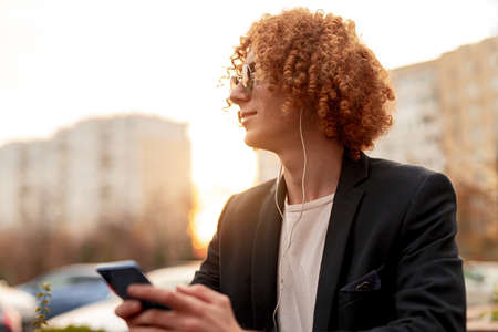Trendy man with smartphone and earphones resting on street
