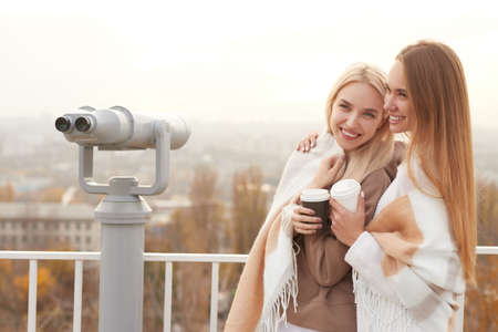 Happy girlfriends with coffee standing on observation deckの写真素材