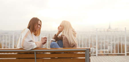Young women with coffee talking on benchの写真素材