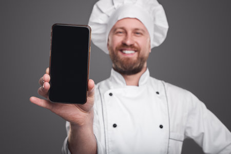 Happy chef showing smartphone at cameraの写真素材