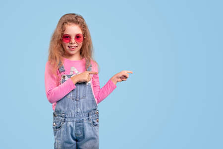 Stylish little girl in sunglasses pointing asideの写真素材