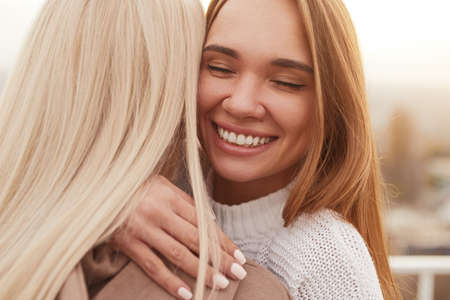 Happy young female best friends hugging on street
