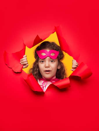 Curious superhero girl looking through hole in paperの写真素材