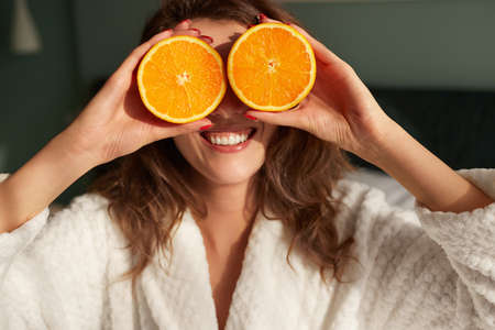 Cheerful woman covering eyes with orange halves