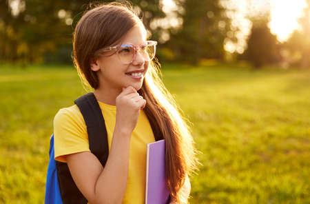 Cheerful schoolgirl in glasses standing in park