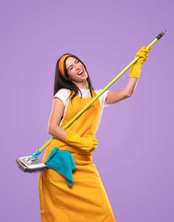 Cheerful female housekeeper having fun with broom in studio