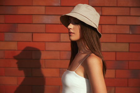 Stylish millennial woman in hat standing near brick wallの写真素材