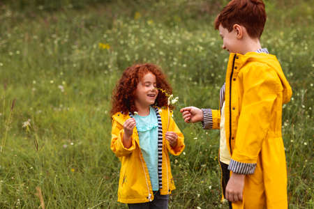 Happy redhead siblings in raincoats enjoying summer day in field