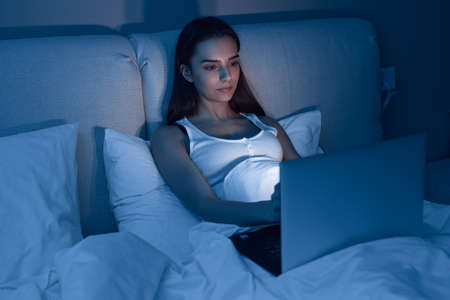 Young woman using laptop in bed at nightの写真素材