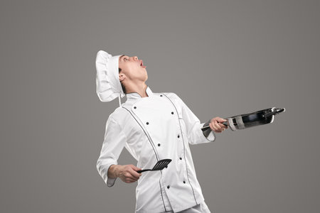 Funny chef with frying pan and spatula looking upの写真素材