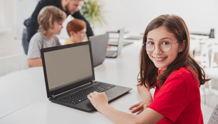 Cheerful schoolgirl with laptop in classroom