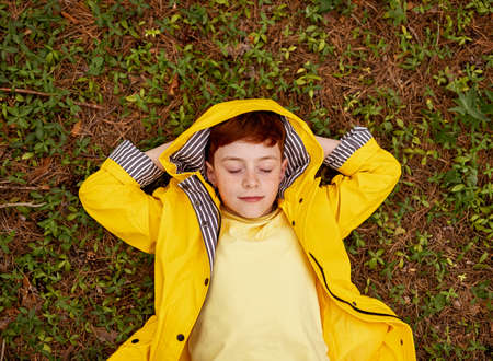 Carefree kid in raincoat lying on grassの写真素材