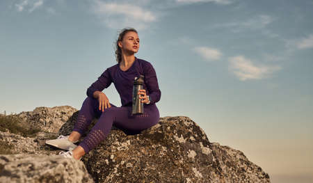 Fit woman with bottle of water resting in nature