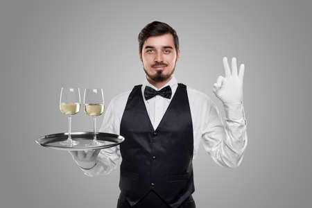 Smiling waiter with glasses of wine showing OK gestureの写真素材