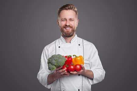 Smiling chef with fresh vegetables on gray backgroundの写真素材