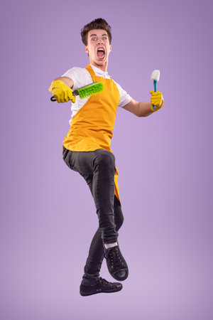 Crazy housekeeper with brushes jumping in studioの写真素材