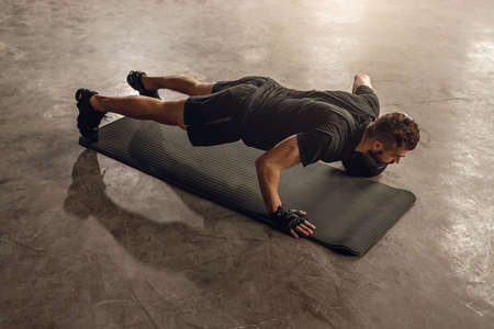 Strong sportsman pushing up on mat in gym
