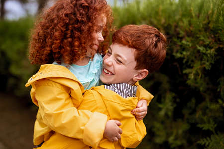 Brother and sister in yellow raincoats embracingの写真素材