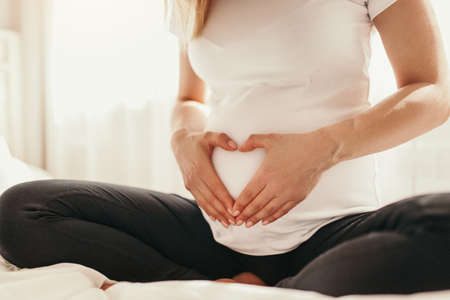 Crop pregnant woman showing heart gesture on her bellyの写真素材
