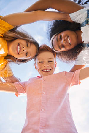 Happy diverse kids hugging against skyの写真素材