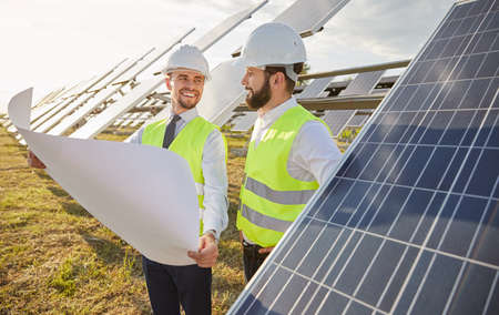 Smiling workers with blueprint in field with solar panelsの写真素材