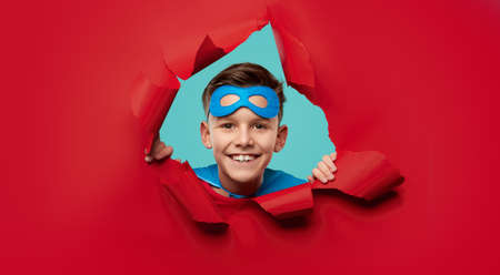 Smiling superhero boy looking through torn paperの写真素材