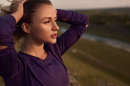 Dreamy young lady touching hair and admiring nature at sunsetの写真素材
