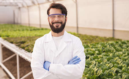 Cheerful man in eyeglasses standing in greenhouseの写真素材