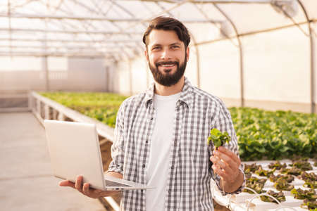 Smiling farmer with laptop in greenhouseの写真素材