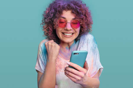 Woman in Holi colors reading god news on cellphoneの写真素材