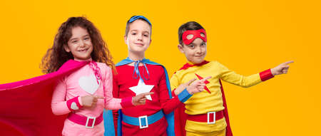 Happy superhero kids pointing away in studioの写真素材