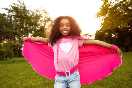Happy black girl in superhero costume in parkの写真素材