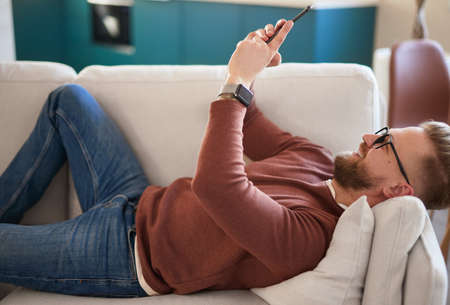 Cheerful man browsing smartphone on sofaの写真素材