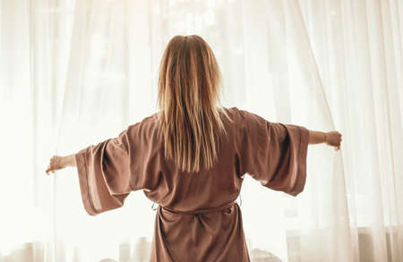 Woman waking up and opening curtainsの写真素材