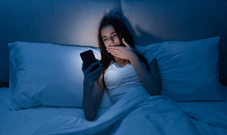 Sleepy female using cellphone in bed at night