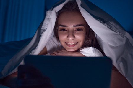 Woman watching movie on tablet under blanketの写真素材