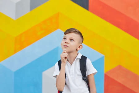 Thoughtful schoolboy looking up against colorful wallの写真素材
