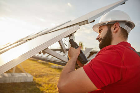 Bearded engineer in hardhat screwing solar panel in field