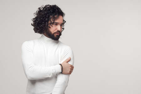 Serious bearded man in white turtleneck touching shoulder in studioの写真素材