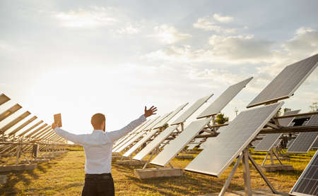Businessman raising arms on spacious solar power farmの写真素材