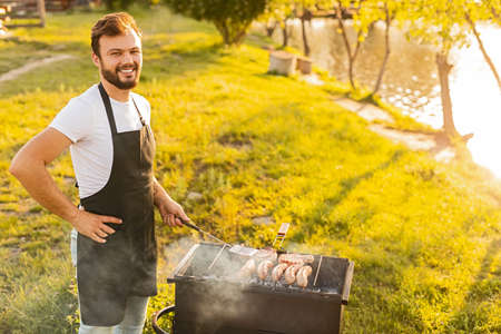 Positive bearded man cooking meat on grillの写真素材