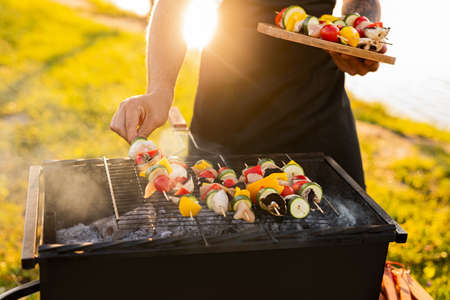 Crop man putting skewers on grill
