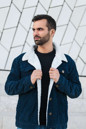 Serious young ethnic man adjusting jacket and looking away on street