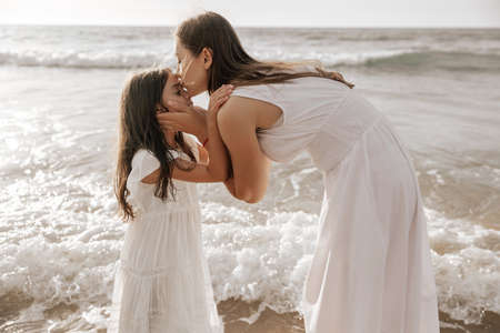 Mother kissing daughter near waving sea