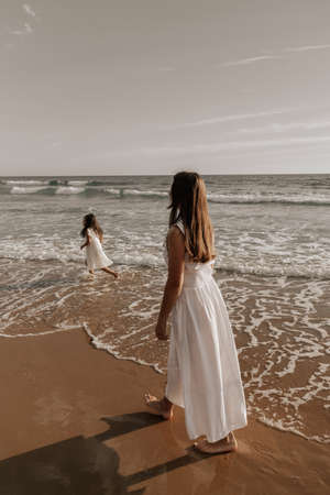 Mother walking near playing daughter on beachの写真素材