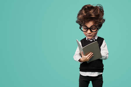 Adorable clever child reading textbook in turquoise studioの写真素材